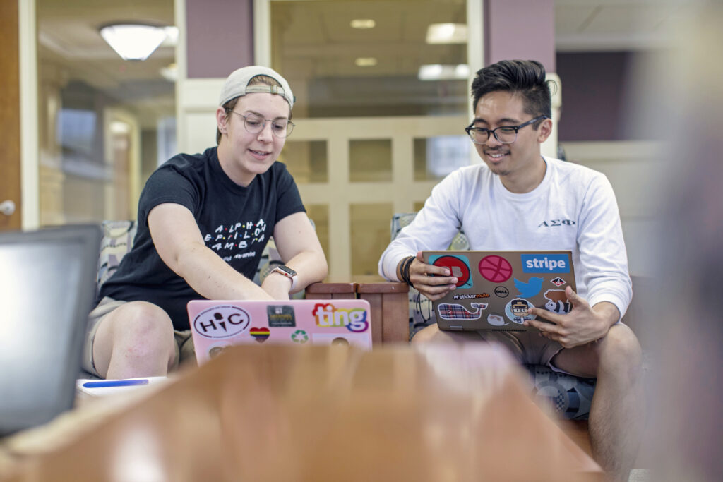 Two students sitting together with laptops.