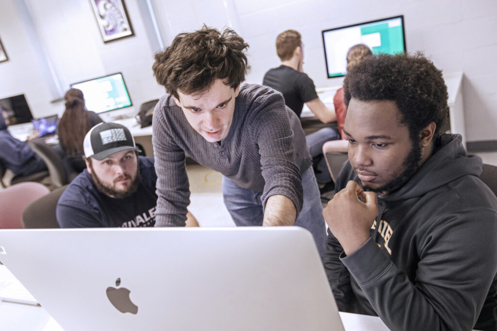 A peer tutor assisting computer science students in a computer lab.