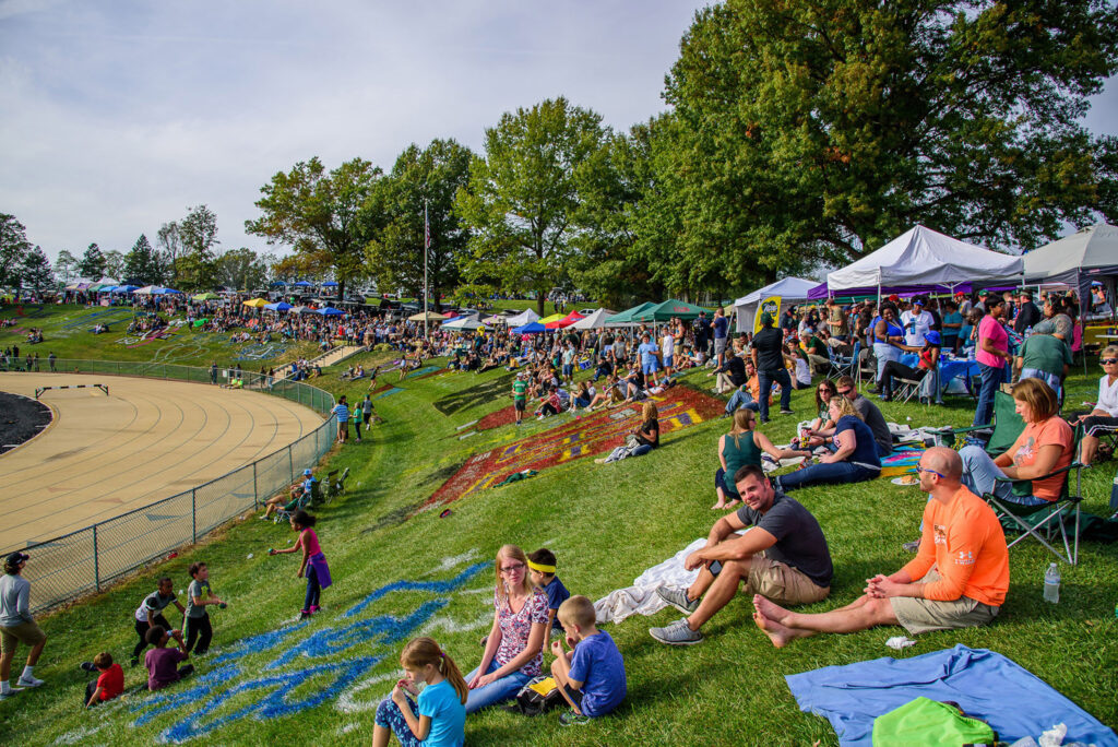 Hundreds of people tailgating at the edge of the football field.